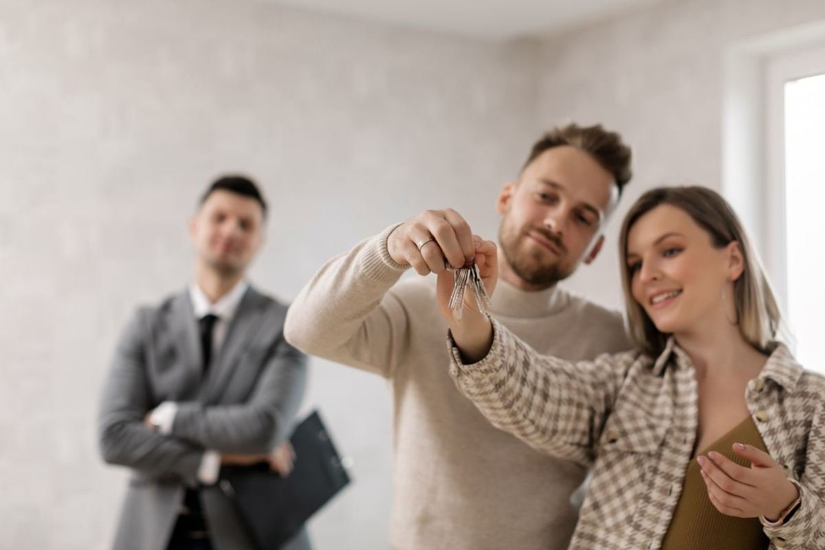 Happy home buyers holding the keys to their new home with their Realtor